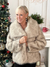 Woman wearing a beige artic faux fur coat in a festive room with Christmas decorations.