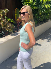 Woman wearing a light green sleeveless top and white pants standing outdoors.