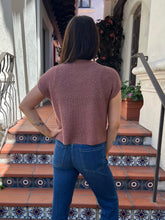A woman viewed from behind wearing a short-sleeve ribbed knit top in a dusty rose pink color, paired with blue jeans, standing on tiled outdoor stairs.