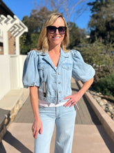 Woman wearing a light blue cropped denim jacket and jeans outdoors on a sunny day.