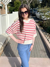 Woman wearing a red and white striped sweater and blue jeans standing outdoors.