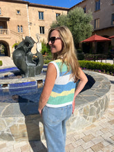 Woman standing in front of a sculpture in an outdoor setting with a building and trees in the background.
