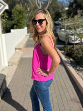 Woman wearing a fuchsia tank top and blue jeans standing outdoors on a patio.