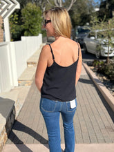 Woman wearing a black tank top and blue jeans with trees in the background.