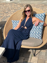 Woman in a blue dress sitting on a wicker chair with blue and white chevron pillows outdoors.