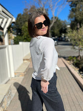 Woman wearing sunglasses and a white blouse with black pinstripe pants outdoors.