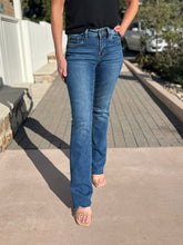Person wearing blue slim bootcut jeans standing on a sidewalk.