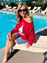 Woman in a red sweatshirt with a sailboat design sitting by a pool.