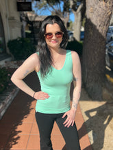 Woman wearing a mint tank top and black pants standing outdoors on a sunny day.