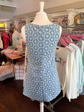 Blue patterned dress on a mannequin in a store setting with racks of clothes in the background.