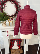Back view of Maroon puffer jacket on a mannequin in front of a festive fireplace with wreath and decorations.