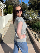 Woman wearing sunglasses and a gray tie  top with blue jeans standing outdoors.