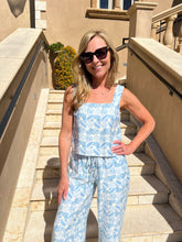 Woman in a blue patterned outfit standing on stone steps outdoors.