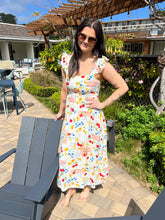 Woman in a colorful dress standing outdoors near a building with greenery.