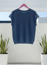 Blue sleeveless knitted top on a hanger with plants in the background