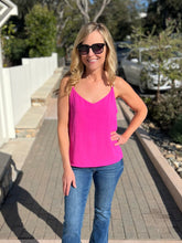 Woman wearing a fuchsia tank top and blue jeans standing outdoors on a patio.