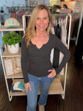 Woman wearing a charcoal long-sleeve top and blue jeans standing in a store.