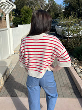 Woman wearing a red and white striped sweater and blue jeans standing outdoors.