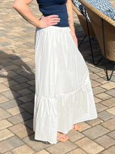 Person wearing a white skirt and navy top on a paved outdoor floor.