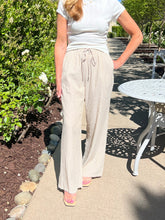 Woman wearing a white top and beige wide-leg pants standing outdoors near a garden and table.