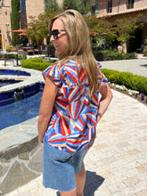 Woman in a colorful shirt and denim shorts standing by a poolside.