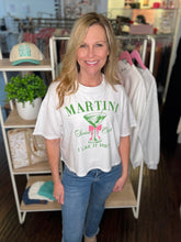 Woman wearing a white t-shirt with green Martini Club text and graphics, standing in a store setting.
