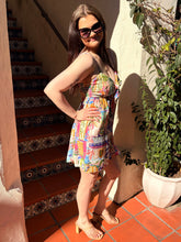 Woman in a colorful mini dress standing on a tiled patio with a plant and staircase in the background