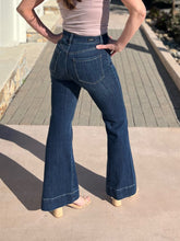 Person wearing blue flared jeans standing on a sidewalk.