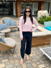 Woman in a pink sweater and black pants standing on a patio with outdoor furniture.
