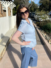 Woman wearing a halogen blue top and pants standing outdoors on a sidewalk.