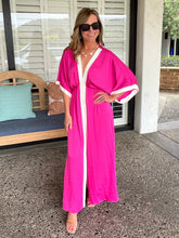 Woman wearing a bright pink robe with white trim standing on a patio.