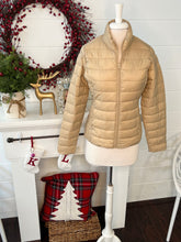 Beige puffer jacket on a mannequin in front of a decorated fireplace.