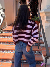 A person viewed from behind wearing a long-sleeve knit sweater with horizontal dark burgundy and light pink stripes, paired with blue jeans, standing on terracotta tiled outdoor stairs.