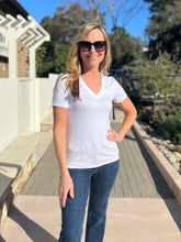 Woman wearing a white t-shirt and blue jeans standing outdoors on a sunny day.
