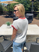 Woman wearing a white shirt with red trim and sunglasses outdoors on a patio.