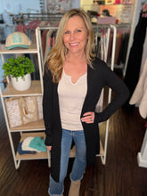 Woman standing in a clothing store wearing a black cardigan, white shirt, and blue jeans.
