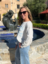 Woman standing in front of a sculpture by a pool with a building and trees in the background