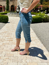 Person wearing blue jeans and clear high-heeled sandals on a paved walkway.