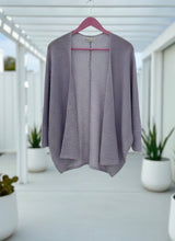 Steel blue cardigan on a hanger with a blurred outdoor background