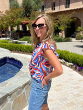 Woman in a colorful shirt and sunglasses standing by a poolside.