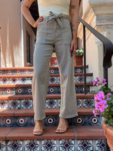 A person wearing light beige high-waisted wide-leg pants with a tie waist, standing on patterned outdoor tiled stairs.