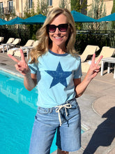 Woman wearing a blue t-shirt with a star design, standing by a pool.