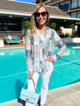 Woman standing by a pool wearing a patterned shirt and sunglasses, with a cow in the background.