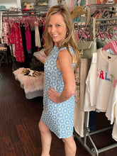 Woman in a blue floral dress standing in a clothing store with racks of clothes in the background.