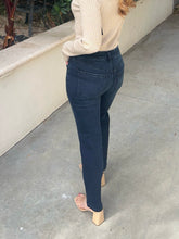 A person shown from the back wearing dark blue skinny jeans, a beige long-sleeve top, and beige block-heel sandals on a concrete patio.