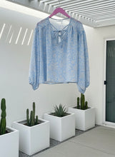 Blue floral tie blouse on a hanger with potted cacti in the foreground