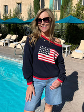 Woman wearing a navy sweater with an American flag design by a poolside.