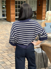 Person wearing a navy and white striped sweater and dark pants outdoors.
