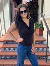 A woman wearing a dark brown cowl-neck sleeveless top and blue jeans, standing on tiled outdoor stairs