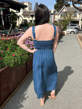 Woman in a dark chambray midi dress standing on a sidewalk with flowers and buildings in the background